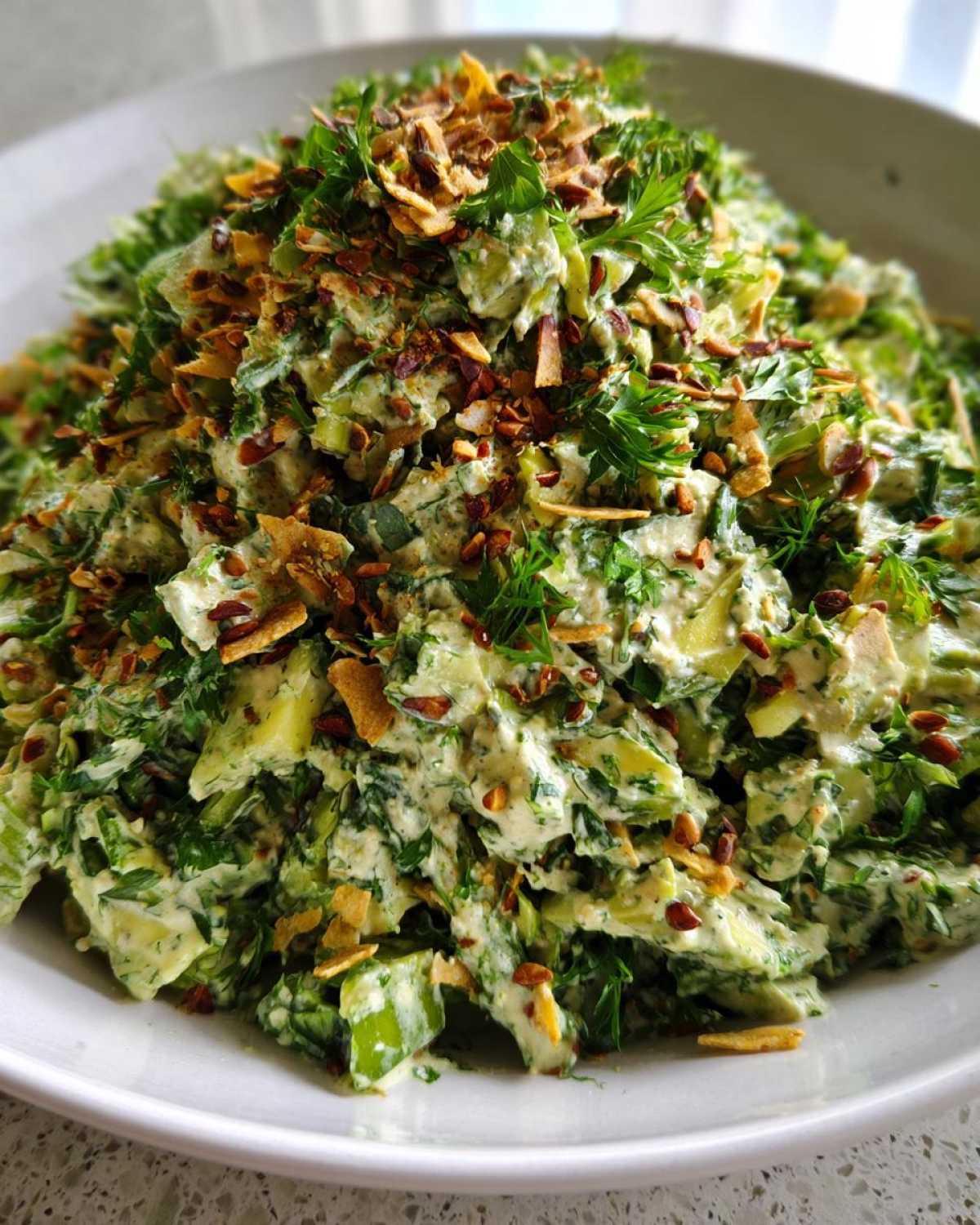 A close-up of the Green Goddess Crunch Salad, heavily coated in creamy dressing and topped with crispy seeds and herbs.