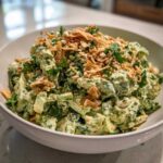A creamy, vibrant Green Goddess Crunch Salad generously topped with crispy fried onions and chopped peanuts in a white bowl.