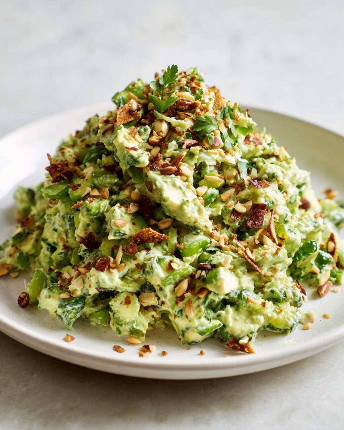 A large mound of creamy Green Goddess Crunch Salad topped with chopped nuts and crispy bacon bits.