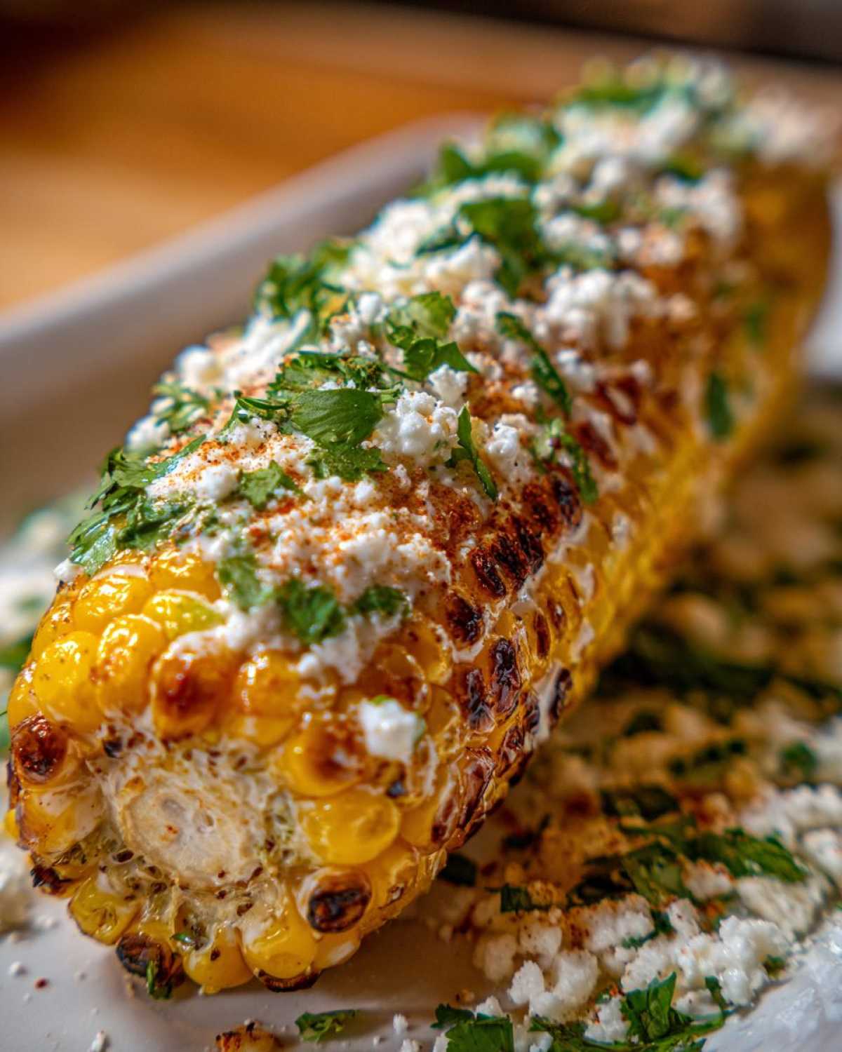 Close-up of a grilled ear of Mexican Street Corn topped with white cheese, cilantro, and chili powder.