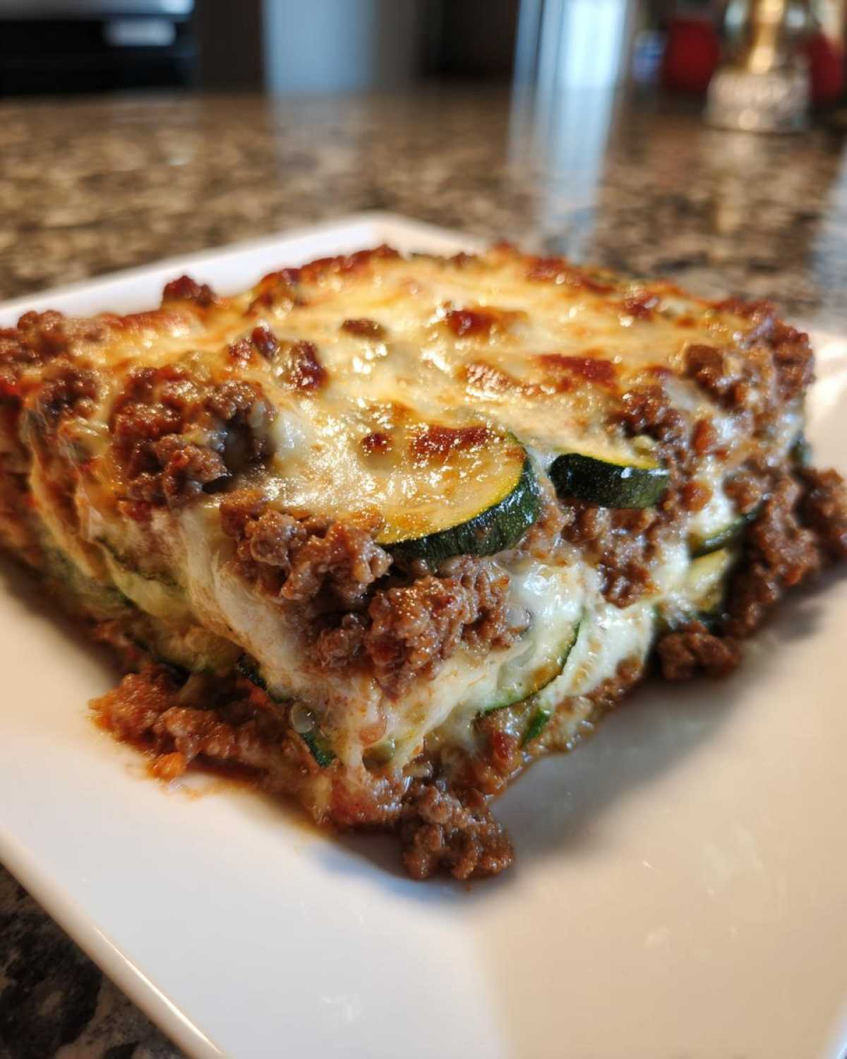 A square serving of cheesy Ground Beef and Zucchini Casserole showing layers of meat sauce and zucchini slices.