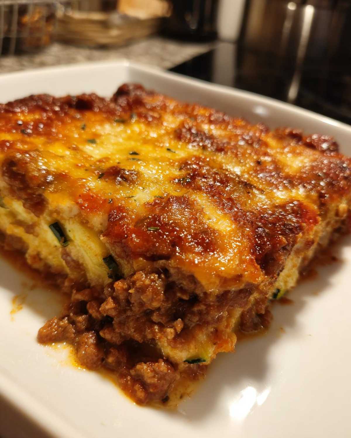 Close-up of a cheesy, baked slice of Ground Beef and Zucchini Casserole on a white plate.
