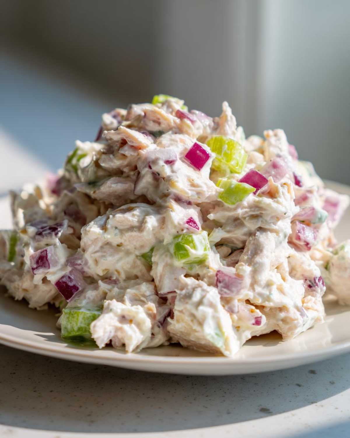 A mound of Healthy Greek Yogurt Chicken Salad mixed with diced red onion and celery on a light plate.