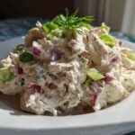 A mound of Healthy Greek Yogurt Chicken Salad mixed with red onion and topped with fresh dill and green onion slices.