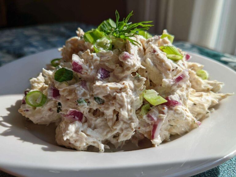 A mound of Healthy Greek Yogurt Chicken Salad mixed with red onion and topped with fresh dill and green onion slices.