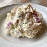 Close-up of a scoop of Healthy Greek Yogurt Chicken Salad mixed with red onion and celery on a white plate.