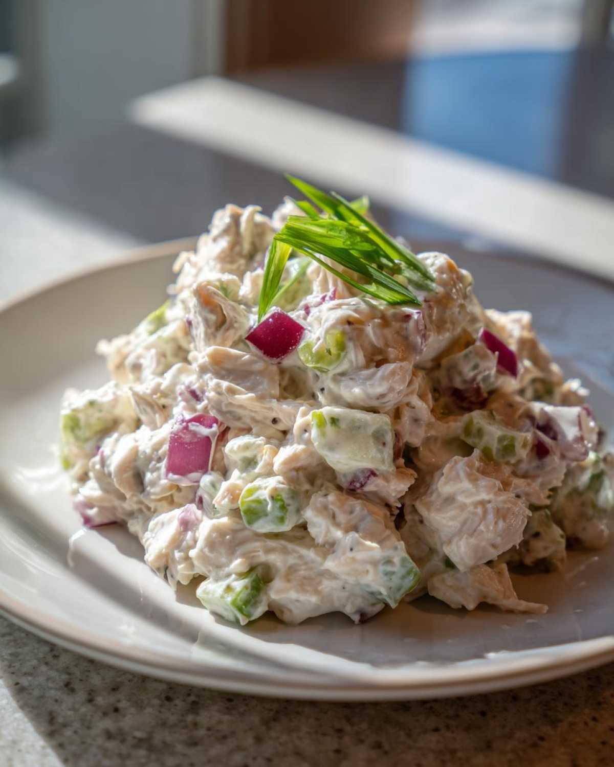 A mound of Healthy Greek Yogurt Chicken Salad with visible chunks of chicken, celery, and red onion, garnished with chives.