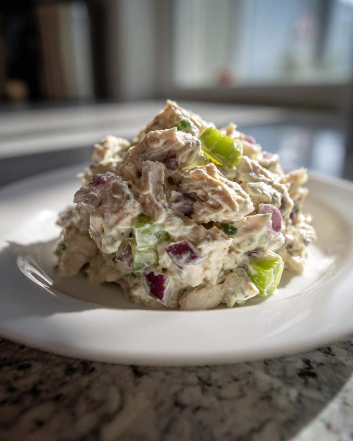 A close-up of a mound of Healthy Greek Yogurt Chicken Salad mixed with red onion and celery on a white plate.