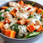 Close-up of a bowl featuring High Protein Sweet Potato Chicken Bowls with chunks of roasted sweet potato, chicken, spinach, and a creamy herb dressing.