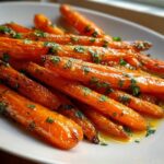 Close-up of glossy Honey Garlic Butter Roasted Carrots sprinkled with fresh parsley on a white serving dish.