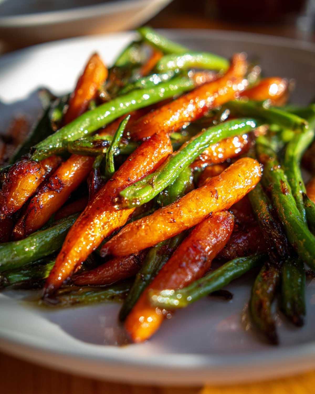 Close-up of vibrant Honey Glazed Carrots and Green Beans glistening with a sweet, dark glaze on a white plate.