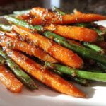A close-up shot of vibrant Honey Glazed Carrots and Green Beans coated in a shiny, sticky sauce on a white plate.