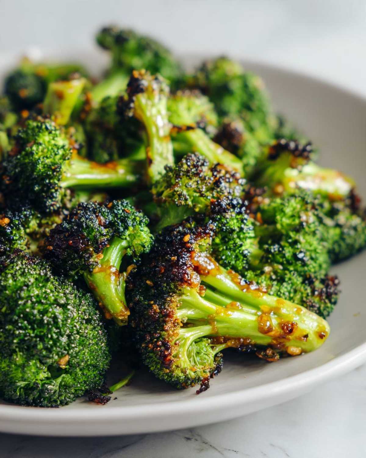 Close-up of vibrant green Honey Mustard Roasted Broccoli florets with caramelized, slightly charred edges on a white plate.
