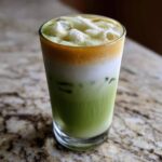 A tall glass of Iced Matcha Latte with Honey Cold Foam showing distinct green, white, and golden-brown layers.