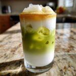 A layered Iced Matcha Latte with Honey Cold Foam featuring green matcha, white milk, and a thick layer of golden foam on top.