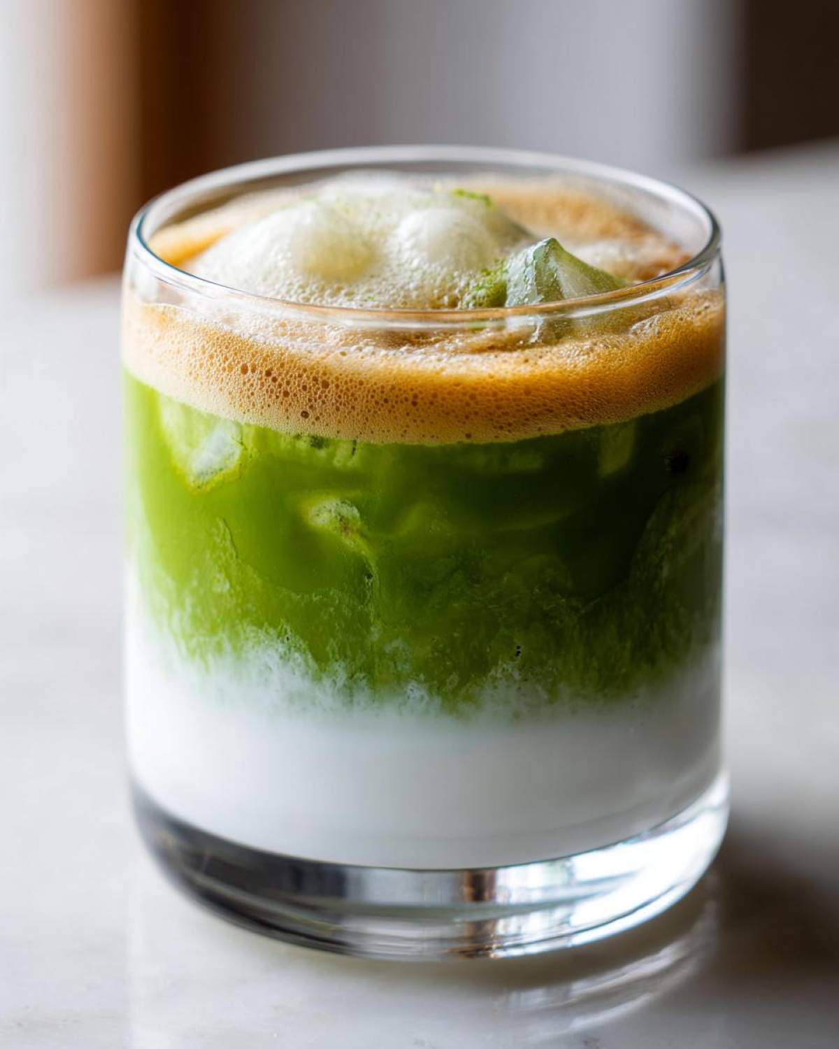 Close-up of an Iced Matcha Latte with Honey Cold Foam showing distinct layers of milk, green matcha, and frothy topping.