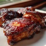 Close-up of three pieces of incredibly juicy bbq chicken coated in a thick, dark, glossy sauce.