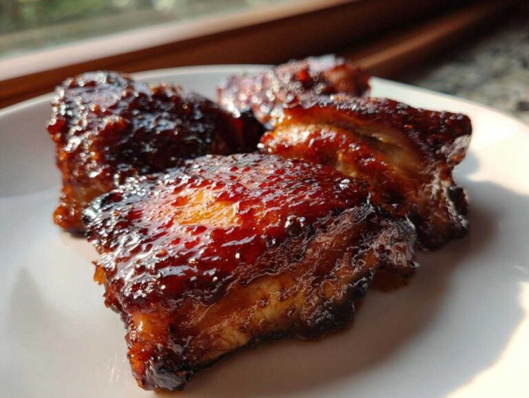 Close-up of three pieces of incredibly juicy bbq chicken coated in a thick, dark, glossy sauce.
