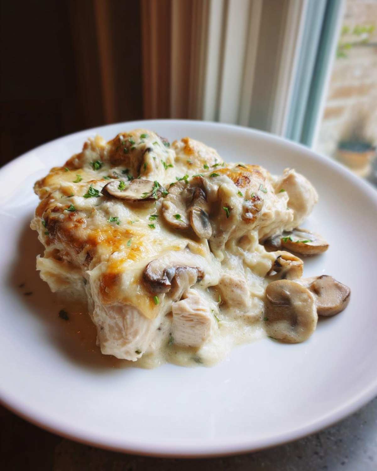 A generous serving of creamy keto garlic mushroom chicken casserole topped with melted cheese and parsley.