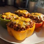 Four colorful Keto Stuffed Bell Peppers filled with ground meat mixture and topped with melted cheddar cheese, served on a white plate.