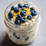 Close-up of Lemon Blueberry Overnight Oats in a jar, topped with fresh blueberries and lemon zest.