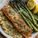 Close-up of a Lemon Herb Roasted Salmon & Asparagus Bowl featuring salmon over quinoa with roasted asparagus and lemon wedges.