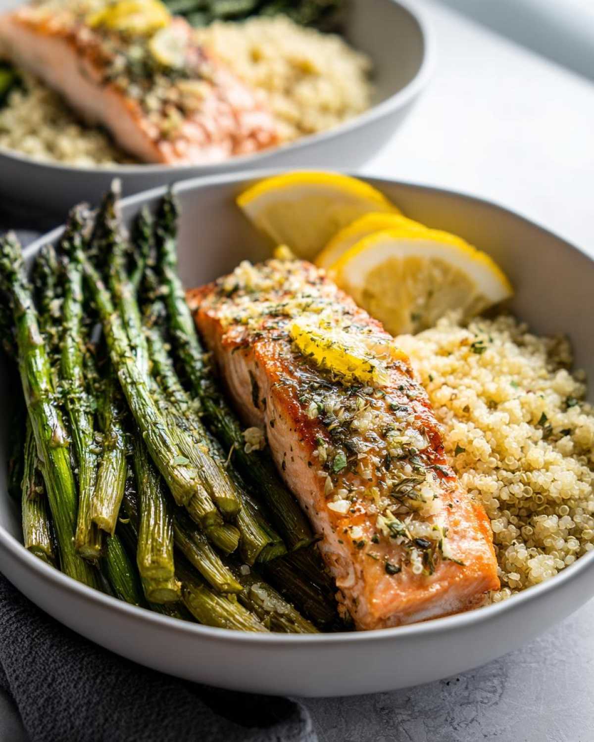 Close-up of a Lemon Herb Roasted Salmon & Asparagus Bowl featuring a piece of seasoned salmon, roasted asparagus, and quinoa.