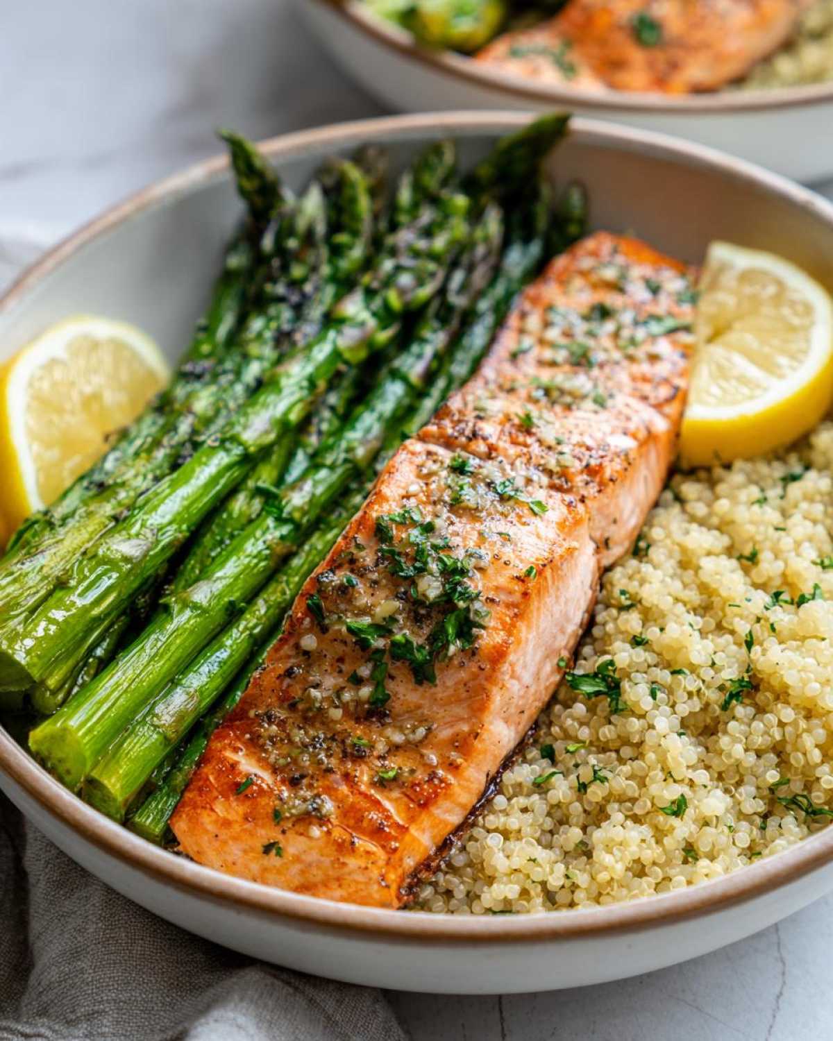 Close-up of a Lemon Herb Roasted Salmon & Asparagus Bowls serving with quinoa and lemon slices.