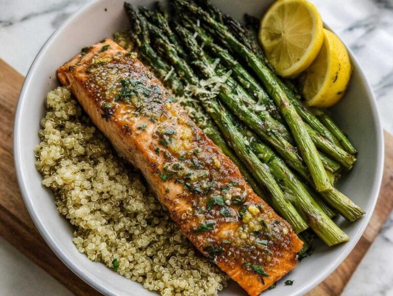 Amazing 15-Minute Lemon Herb Roasted Salmon Bowls Close-up of a Lemon Herb Roasted Salmon & Asparagus Bowl featuring salmon over quinoa with roasted asparagus and lemon wedges.