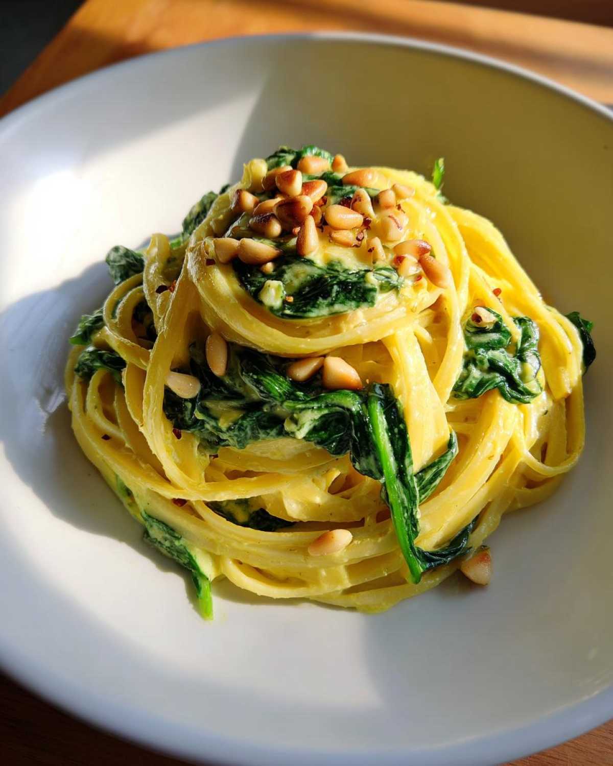 A serving of creamy Lemon Ricotta Pasta with Spinach, topped with toasted pine nuts.