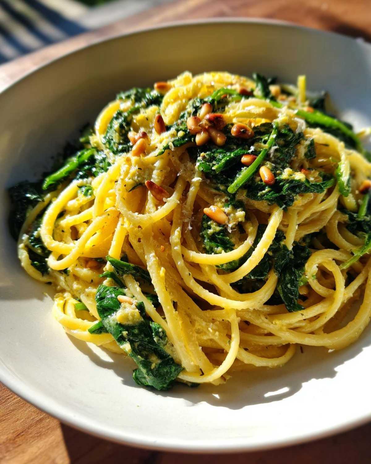 A close-up serving of Lemon Ricotta Pasta with Spinach, coated in a creamy sauce and topped with toasted pine nuts.