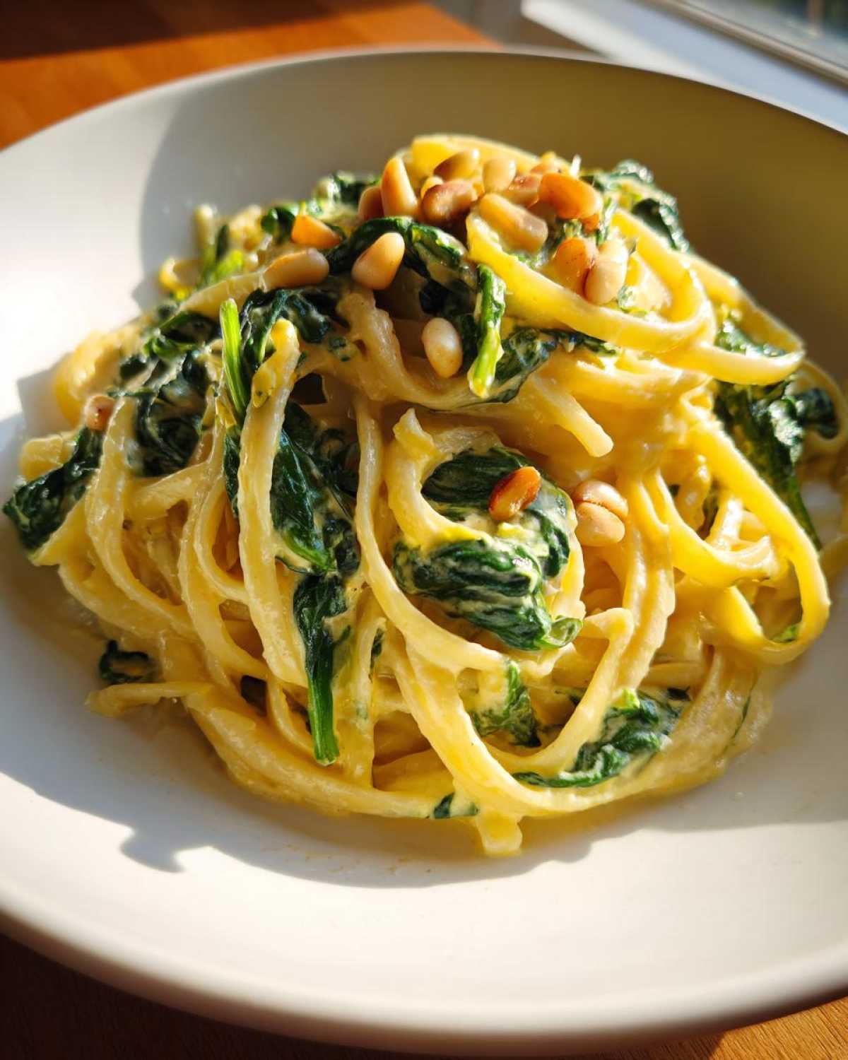 A creamy serving of Lemon Ricotta Pasta with Spinach, topped with toasted pine nuts, bathed in sunlight.