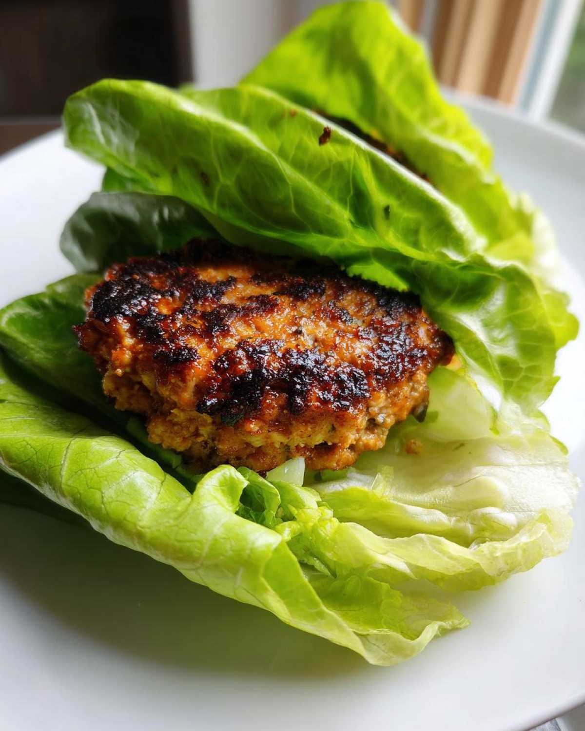 Close-up of a juicy, seared Lettuce Wrap Turkey Burger nestled inside crisp green lettuce leaves.