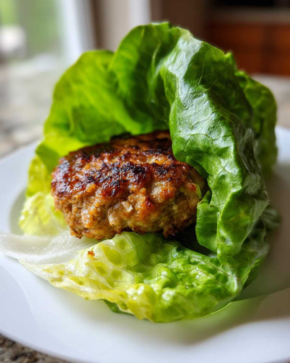 Close-up of a perfectly seared turkey burger nestled inside bright green lettuce leaves for a Lettuce Wrap Turkey Burgers.