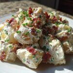 A serving of creamy Loaded Baked Potato Salad topped generously with crispy bacon bits and fresh green chives.
