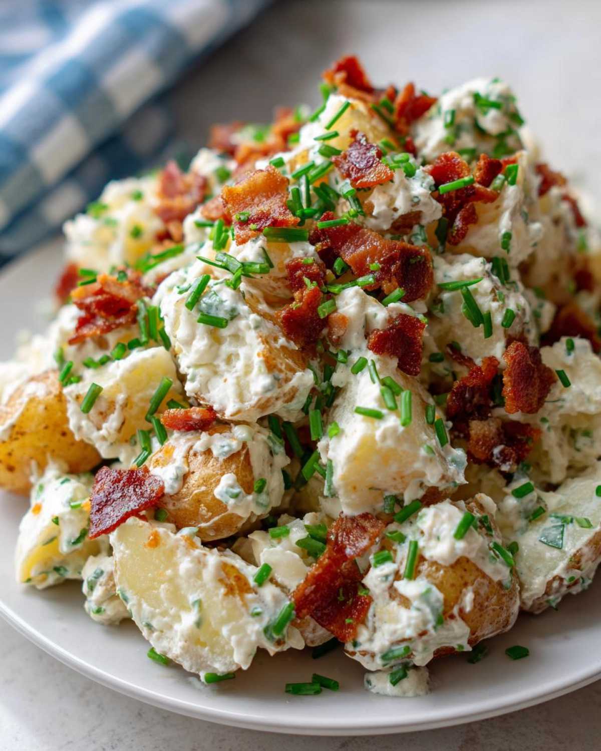 Close-up of a generous serving of Loaded Baked Potato Salad, featuring creamy dressing, chunks of potato, crispy bacon, and fresh chives.