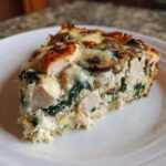 A close-up slice of Low-Carb Chicken Spinach Mushroom Casserole showing chunks of chicken, spinach, and melted cheese topping.