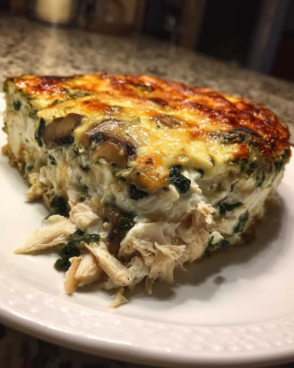 A close-up of a hearty slice of Low-Carb Chicken Spinach Mushroom Casserole with shredded chicken.