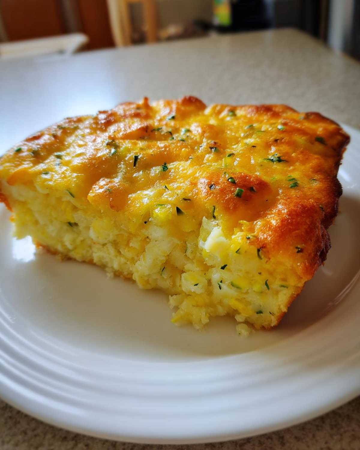 A close-up of a square slice of baked low-carb squash casserole with a golden, melted cheese topping.