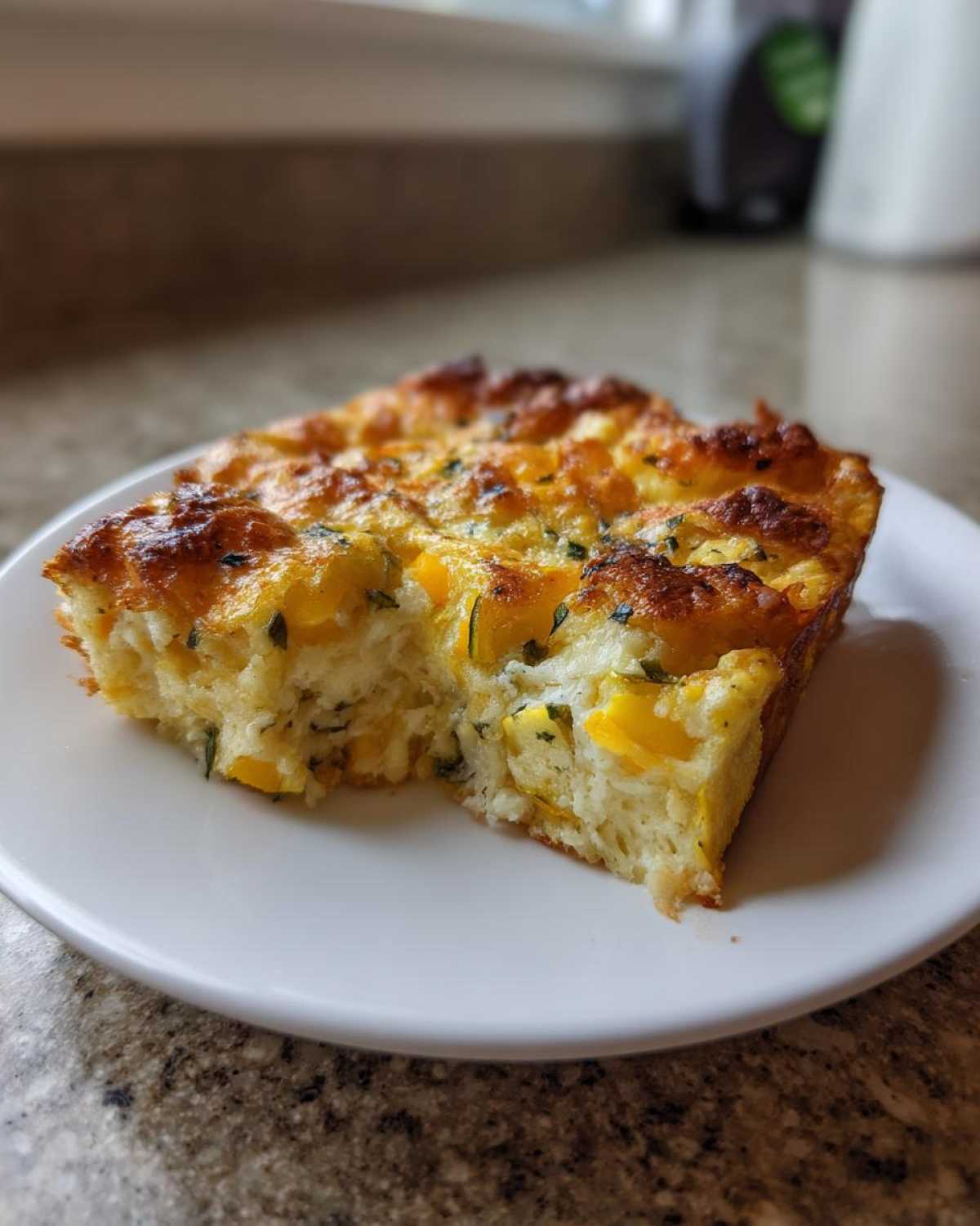 A square slice of baked low-carb squash casserole with a golden-brown, cheesy top, served on a white plate.