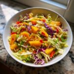 A close-up of a vibrant Mango Habanero Summer Slaw featuring chunks of bright orange mango, shredded green and purple cabbage, and red peppers.