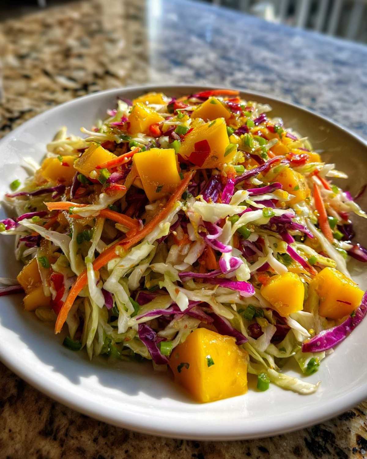 A close-up of vibrant Mango Habanero Summer Slaw featuring shredded cabbage, carrots, and large chunks of bright yellow mango.