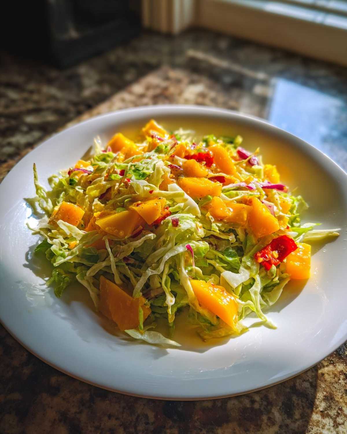 A vibrant serving of Mango Habanero Summer Slaw featuring shredded cabbage and bright orange mango chunks on a white plate.