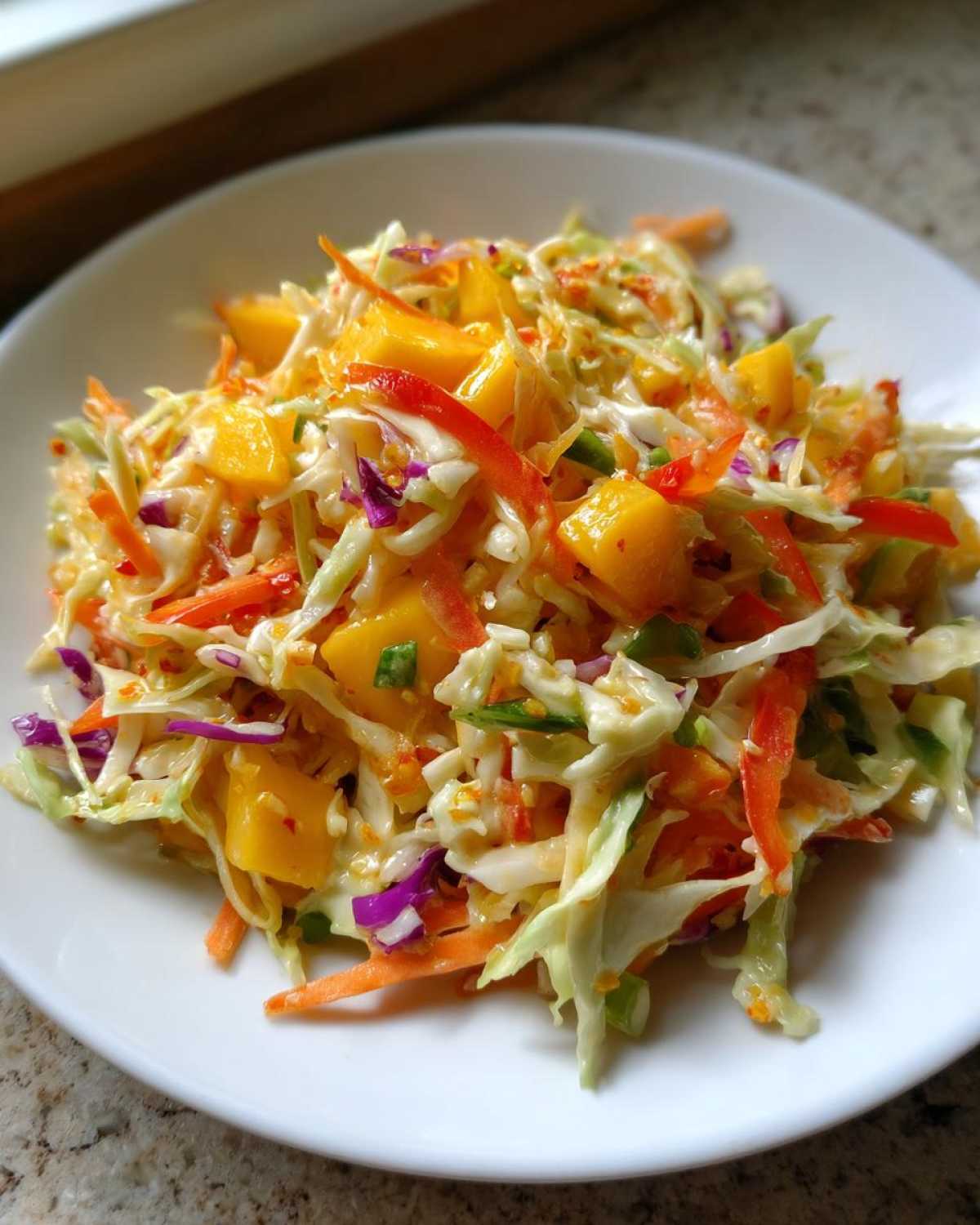 A close-up of vibrant Mango Habanero Summer Slaw featuring shredded cabbage, carrots, and bright yellow mango chunks.