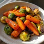 A close-up shot of roasted baby carrots and Brussels sprouts coated in a shiny glaze, representing Maple Glazed Carrots and Brussels Sprouts.