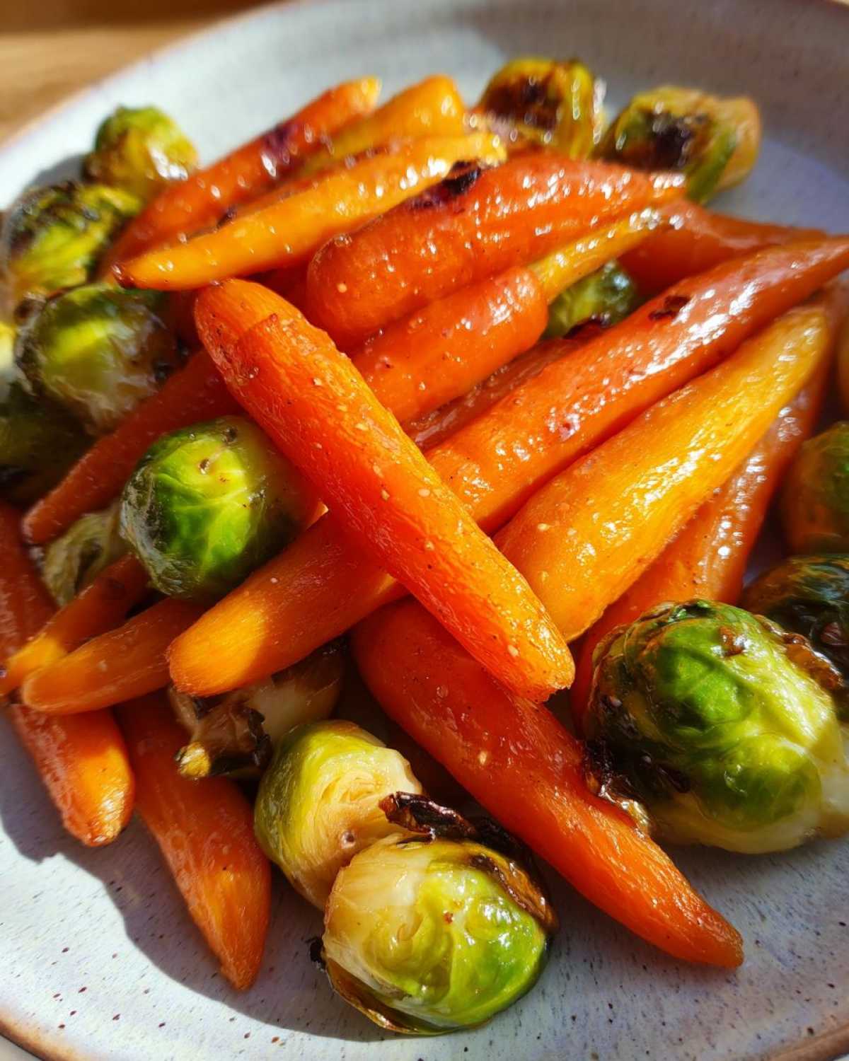 Close-up of vibrant orange carrots and bright green Brussels sprouts coated in a shiny Maple Glazed Carrots and Brussels Sprouts glaze.