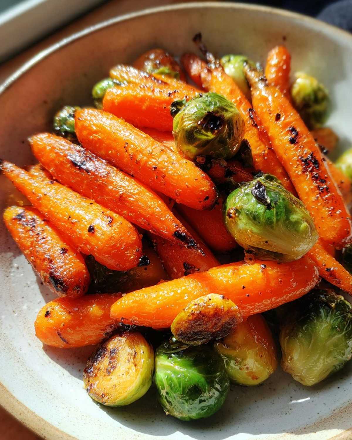 Close-up of bright orange Maple Glazed Carrots and Brussels Sprouts roasted until slightly charred.