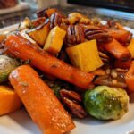 Close-up of glazed Maple Roasted Thanksgiving Veggies including carrots, butternut squash, Brussels sprouts, and pecans.