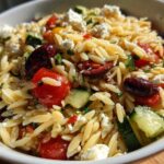 A close-up bowl of vibrant Mediterranean Orzo Salad with Feta, featuring orzo pasta, cherry tomatoes, cucumber, Kalamata olives, and crumbled feta.