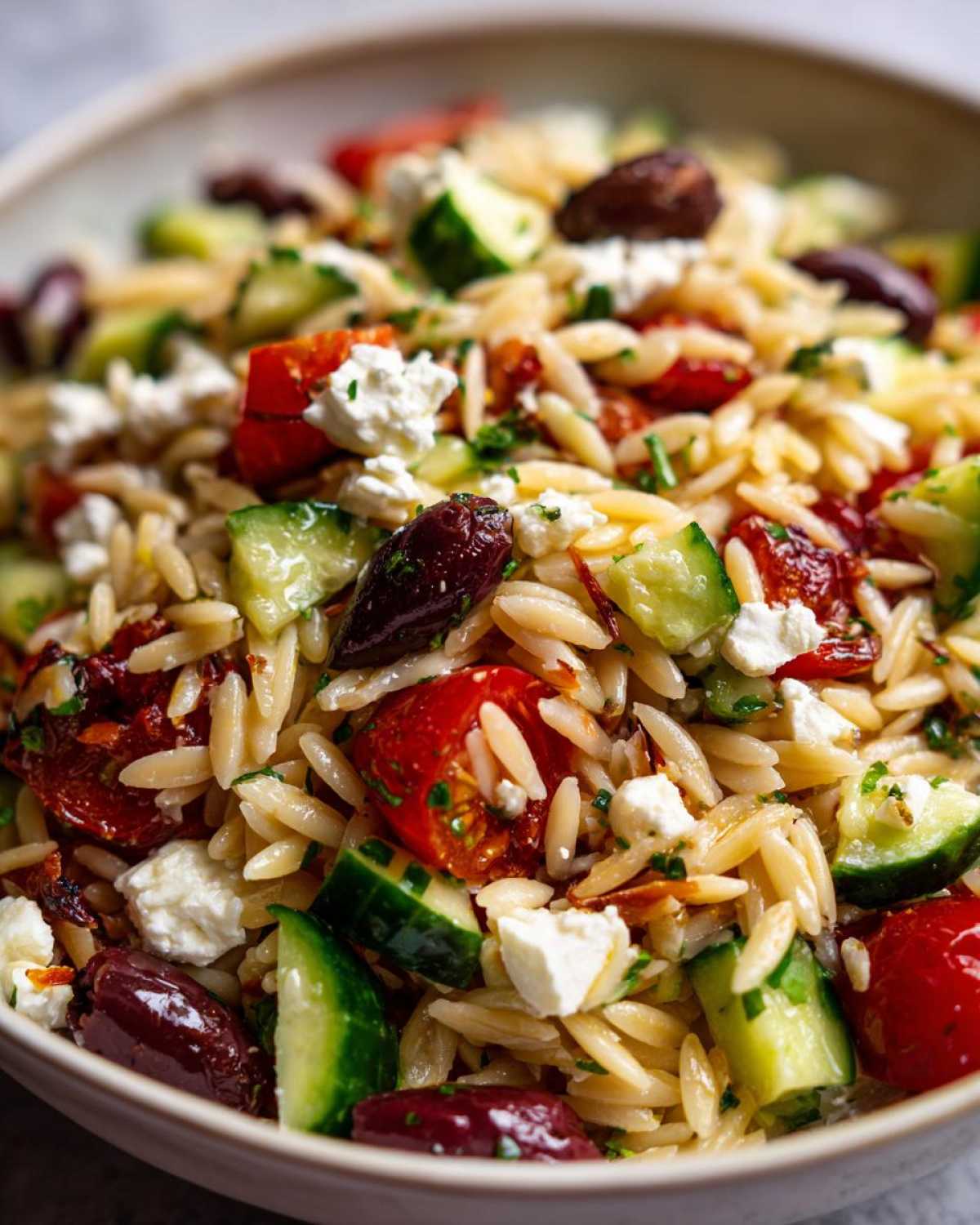 Close-up of a bowl filled with Mediterranean Orzo Salad with Feta, featuring orzo pasta, cucumbers, tomatoes, olives, and feta cheese.